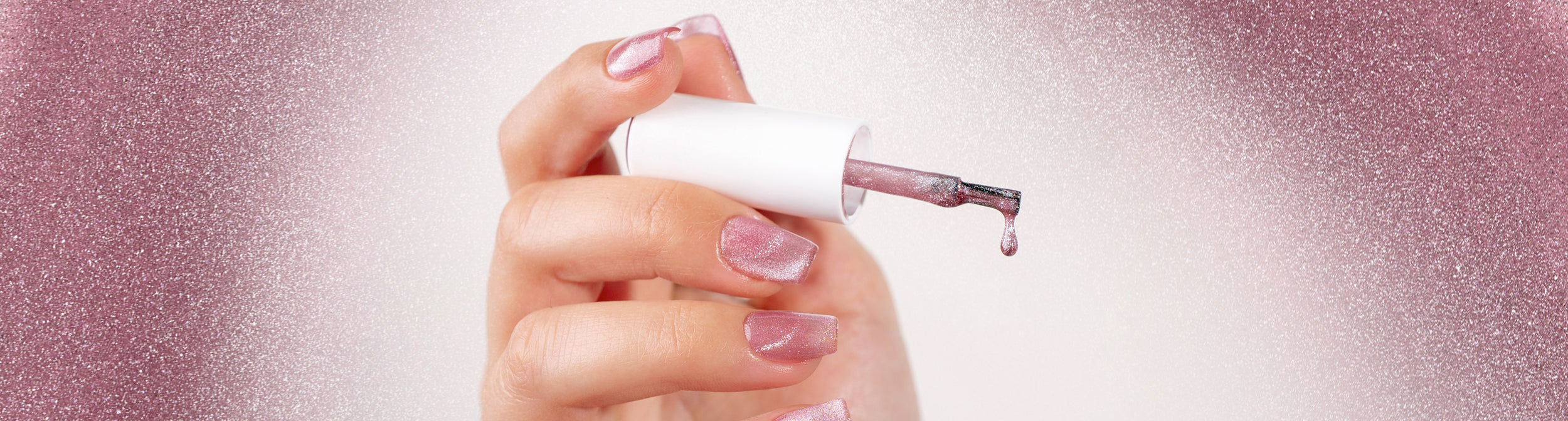 Uñas con esmalte efecto cat eye rosa brilloso, brocha aplicando esmalte de manicura.