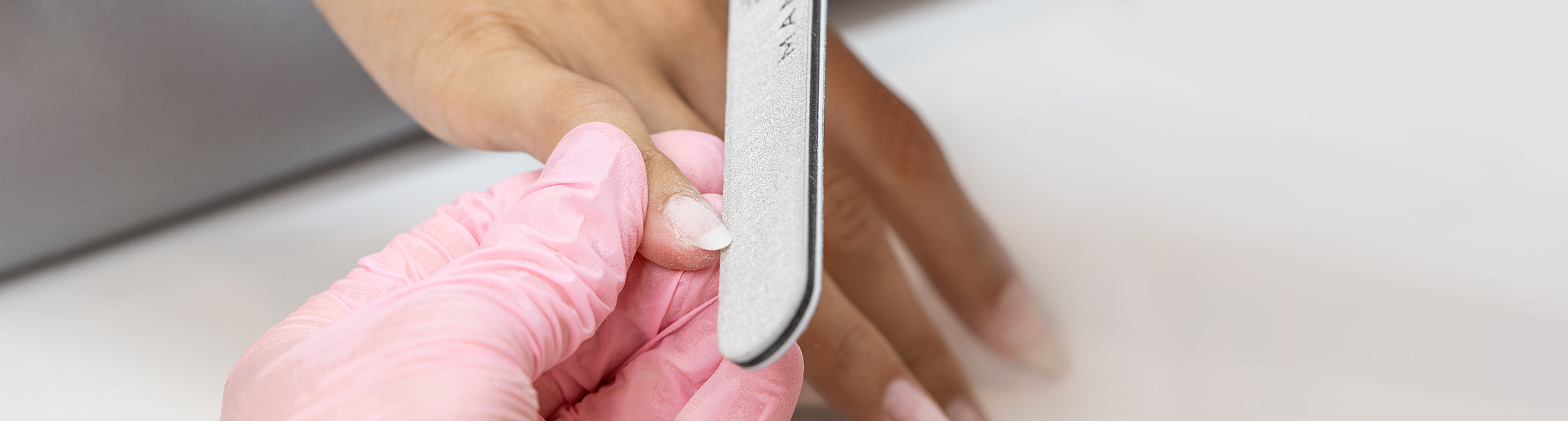 Manicura profesional limando uñas con lima y guantes rosas, cuidado de uñas
