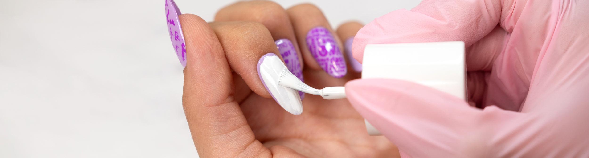 Aplicación de esmalte blanco en uñas decoradas con diseño morado, manicura profesional