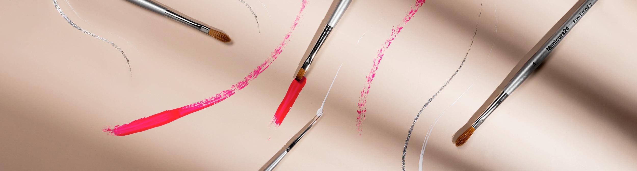 Pinceles para uñas de manicura con trazos de esmalte rosa y plateado sobre fondo beige
