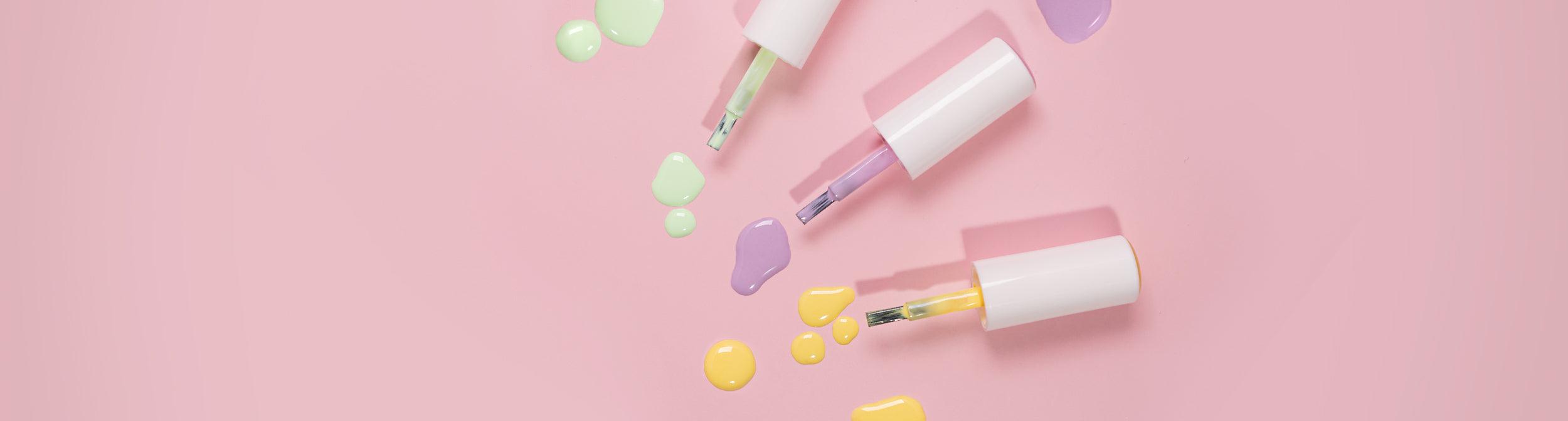 Esmaltes de uñas en tonos pastel y pinceles sobre fondo rosa, productos de manicura