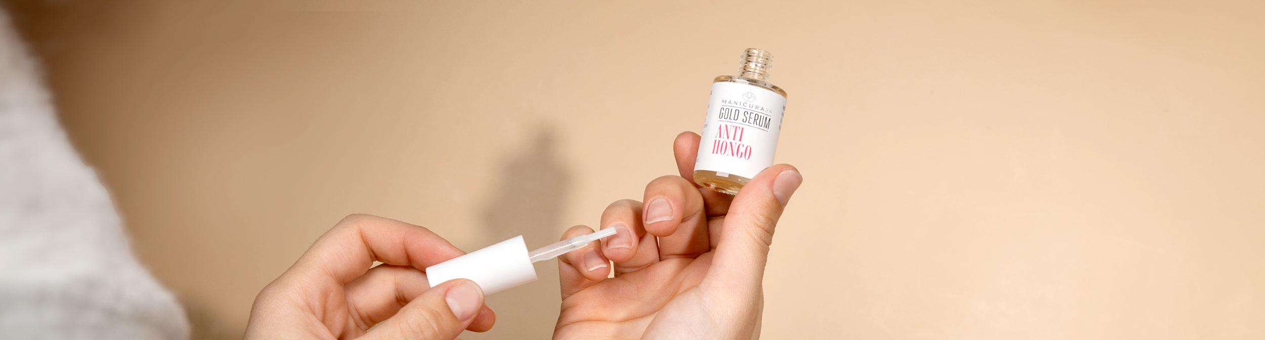 Manos aplicando serum anti-hongos para uñas, producto de manicura sobre fondo beige