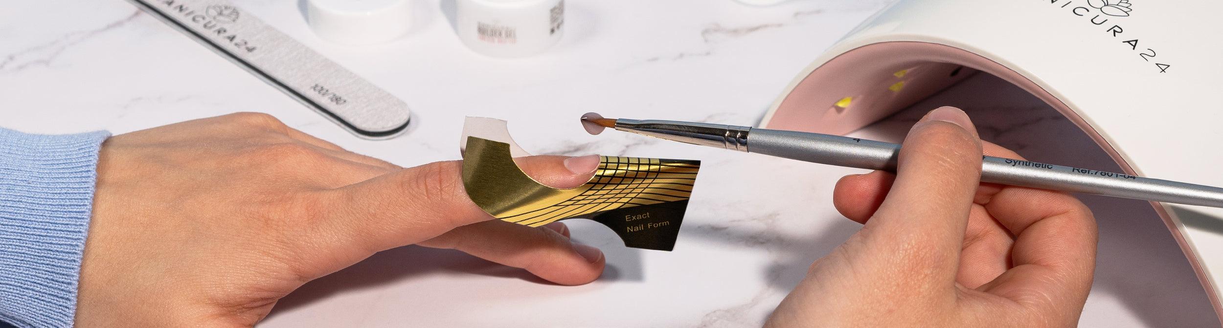 Aplicación de gel para uñas con molde, pincel y lámpara de manicura sobre mesa