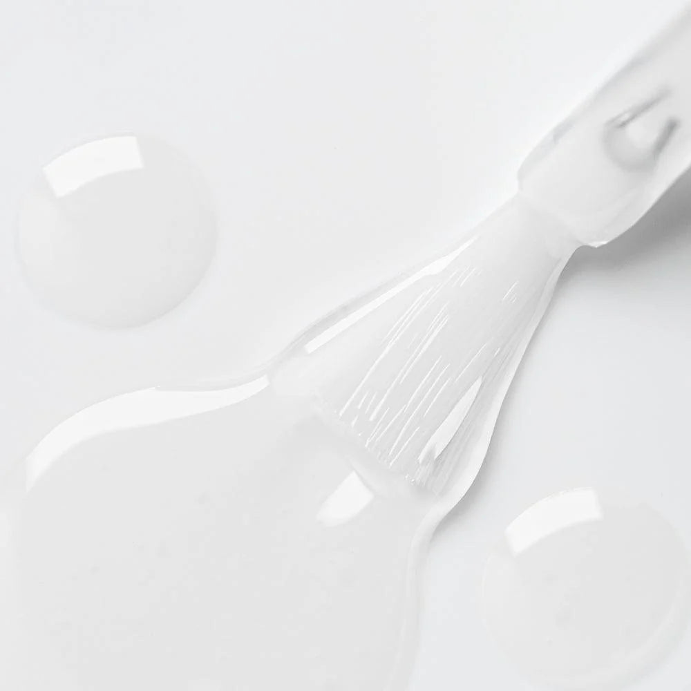 Brocha aplicando gel transparente para uñas sobre superficie blanca