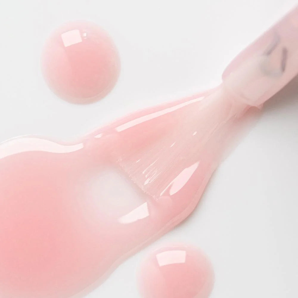 Esmalte de uñas rosa claro aplicado con brocha sobre superficie blanca, producto de manicura.