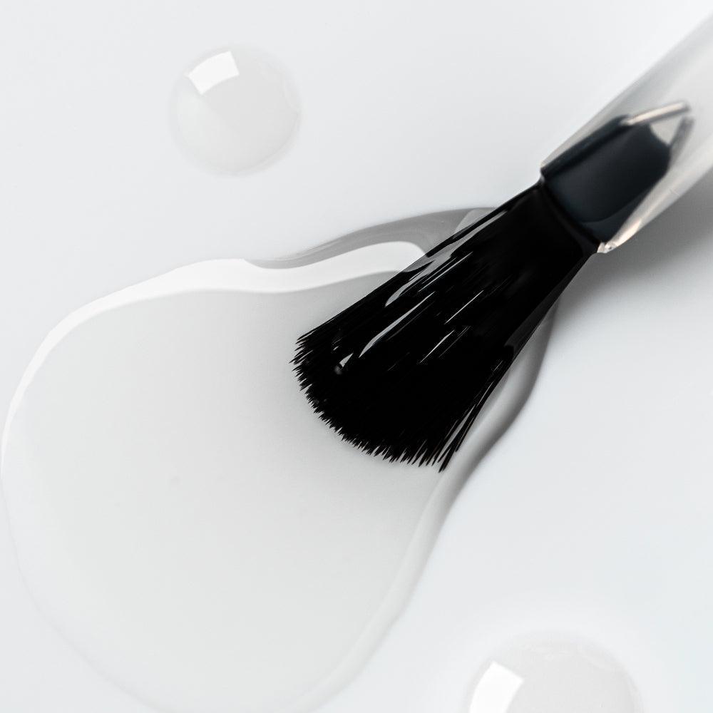 Brocha de manicura con gel transparente sobre fondo blanco, producto de uñas profesional