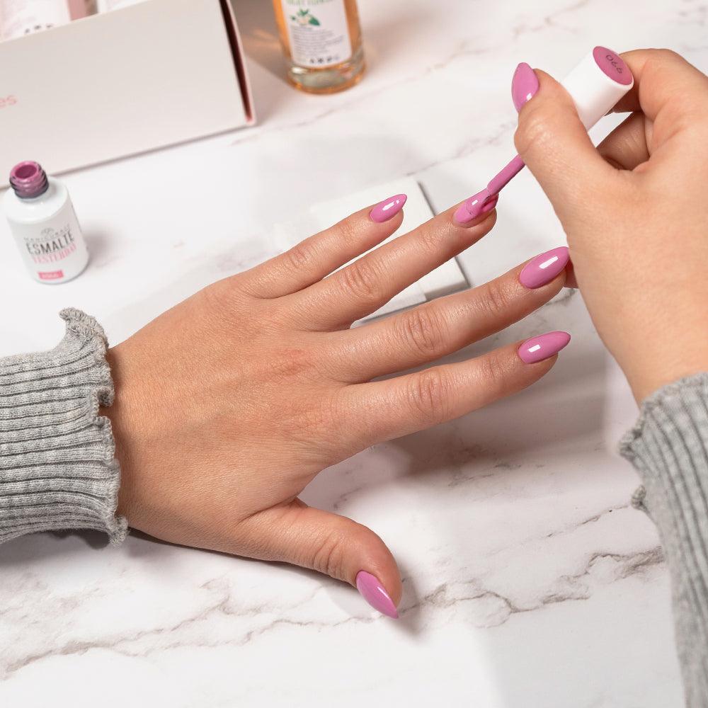 Manicura con esmalte rosa aplicándose en uñas largas sobre fondo de mármol, kit de manicura visible