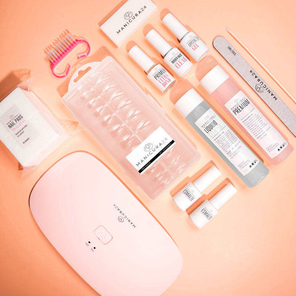 Kit de manicura con lámpara LED, limas, esmaltes, tips de uñas y líquidos sobre fondo rosa.