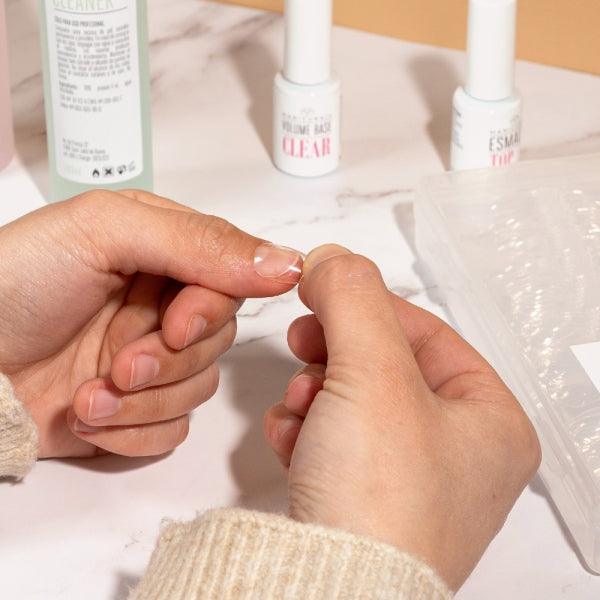 Aplicación de tips de gel en uñas naturales con productos de manicura sobre mesa blanca