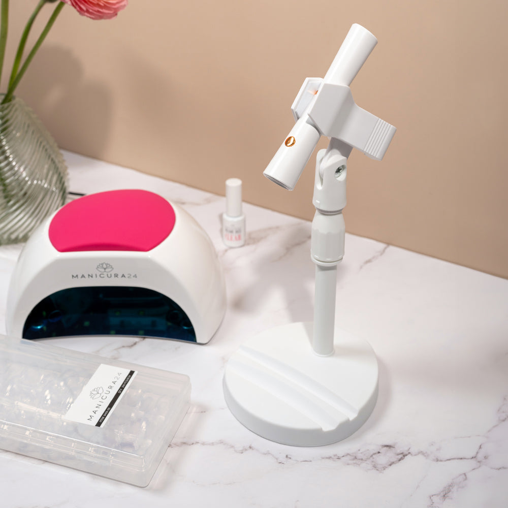 Lámpara de manicura LED con soporte, tips y esmalte sobre mesa de mármol, ambiente profesional.