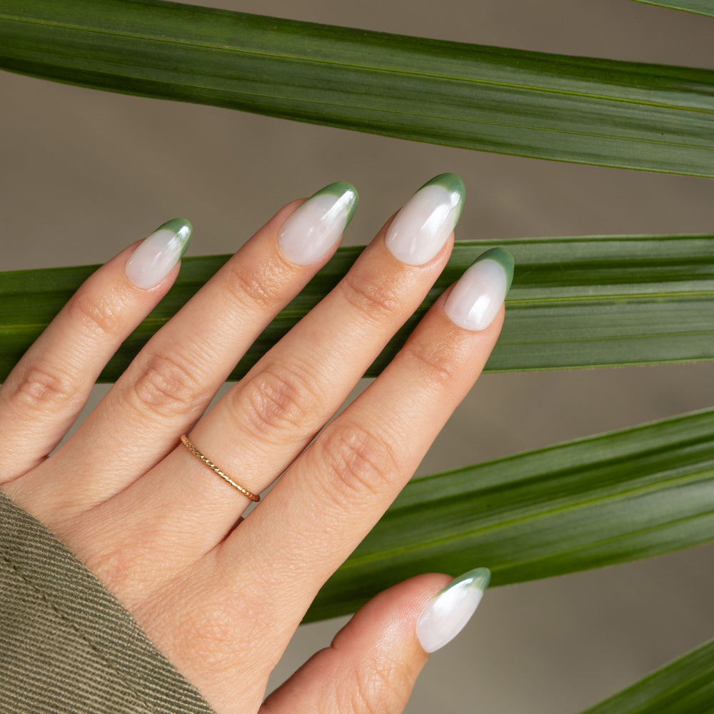Uñas almendradas con manicura francesa verde y fondo de hojas naturales