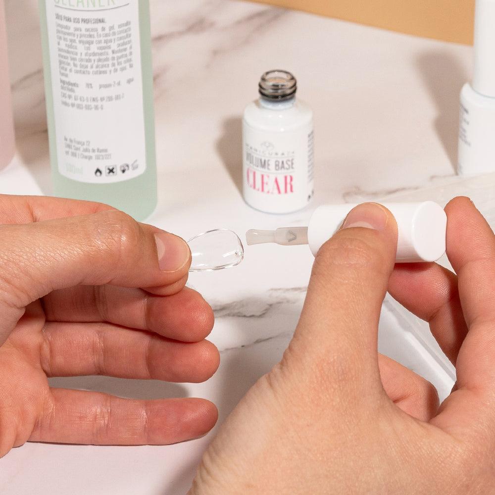 Aplicando base en tips de gel para uñas en kit de manicura sobre mesa de mármol.