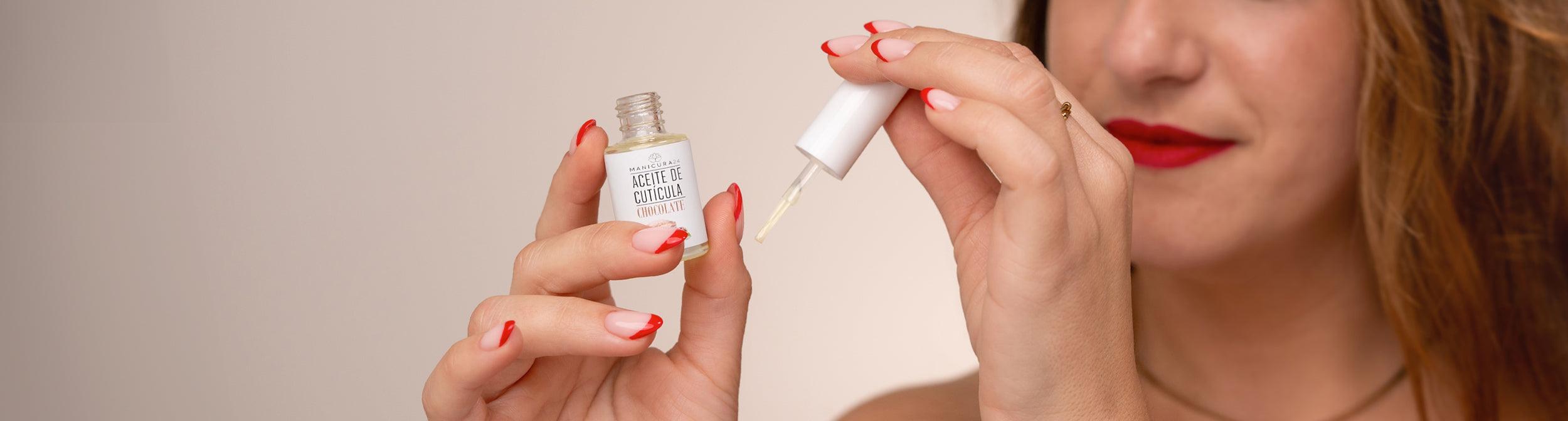 Manos aplicando aceite de cutícula en uñas esmaltadas con diseño rojo, cuidado de uñas