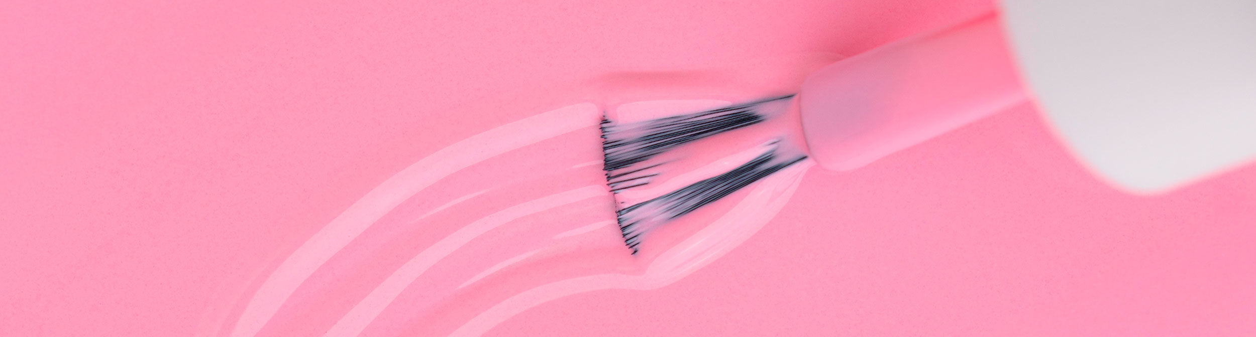 Brocha aplicando esmalte de uñas rosado sobre superficie rosa, manicura profesional