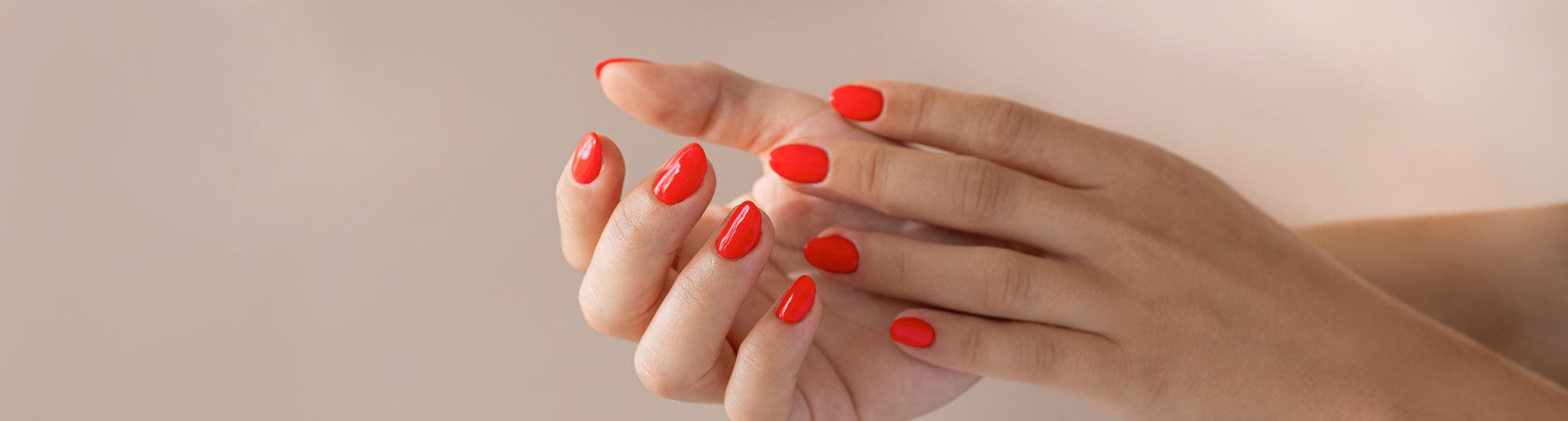 Uñas manicura semipermanente color rojo brillante en manos femeninas bien cuidadas