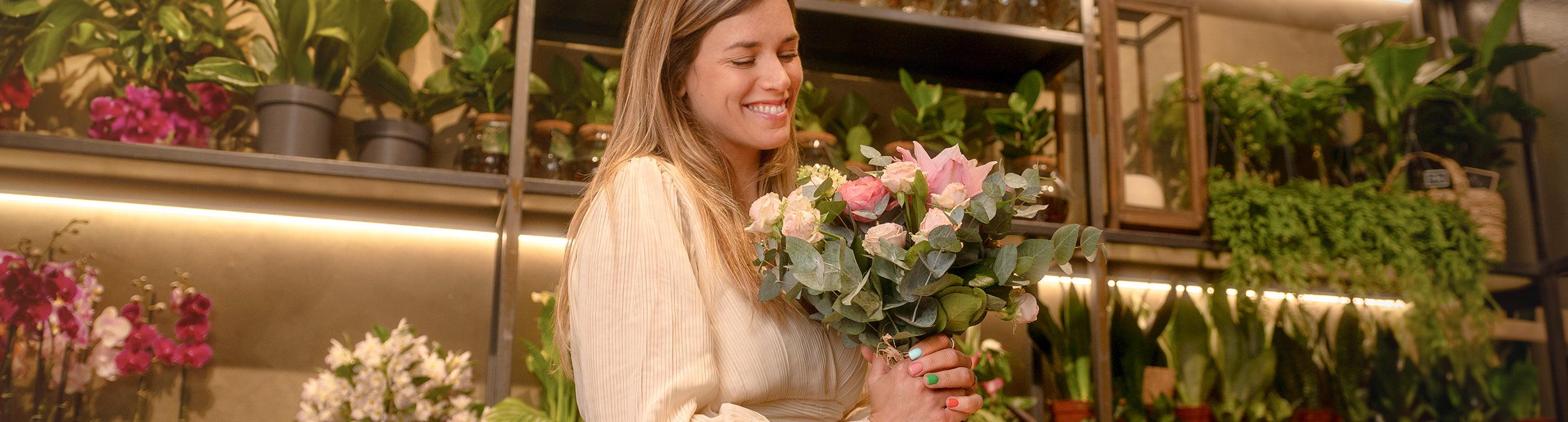 Mujer sonriente con manicura sostiene ramo de flores en tienda de plantas y flores