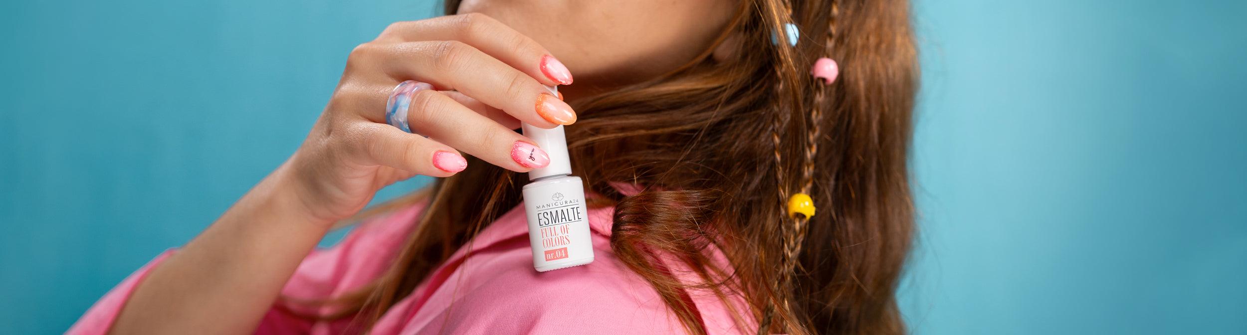 Mano con manicura creativa sosteniendo esmalte semipermanente, fondo azul, cabello con cuentas.