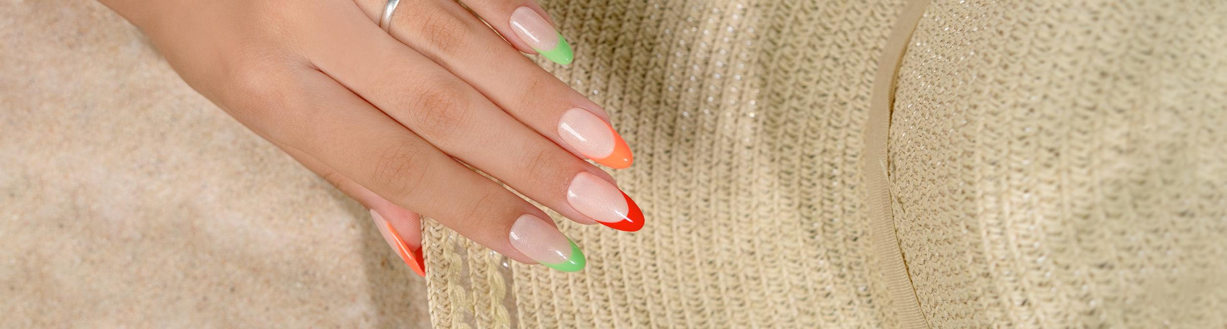 Uñas con manicura francesa colorida en tonos verde y naranja, sobre sombrero de paja.