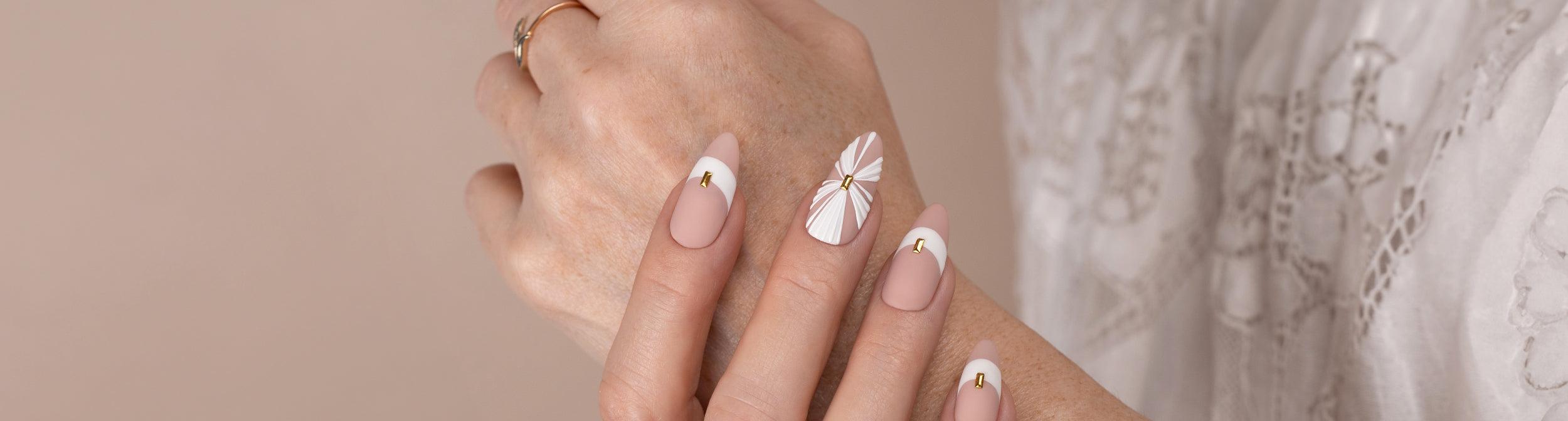 Uñas de manicura elegante para novia con diseño nude y blanco, detalles dorados y decoración floral.