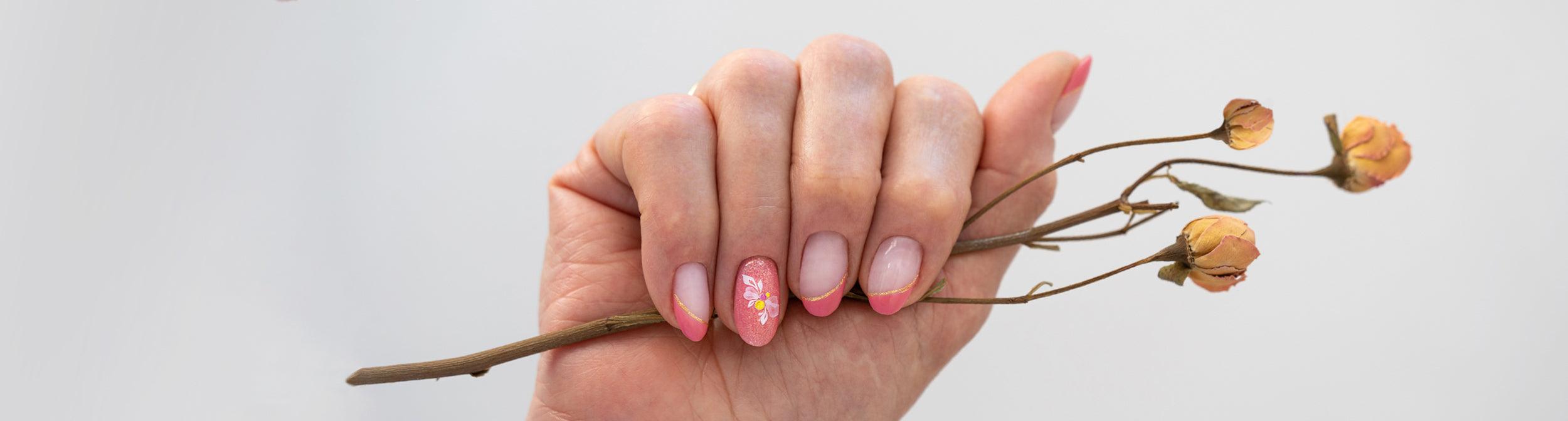 Mano con manicura francesa rosa y arte floral en una uña, sosteniendo flores secas