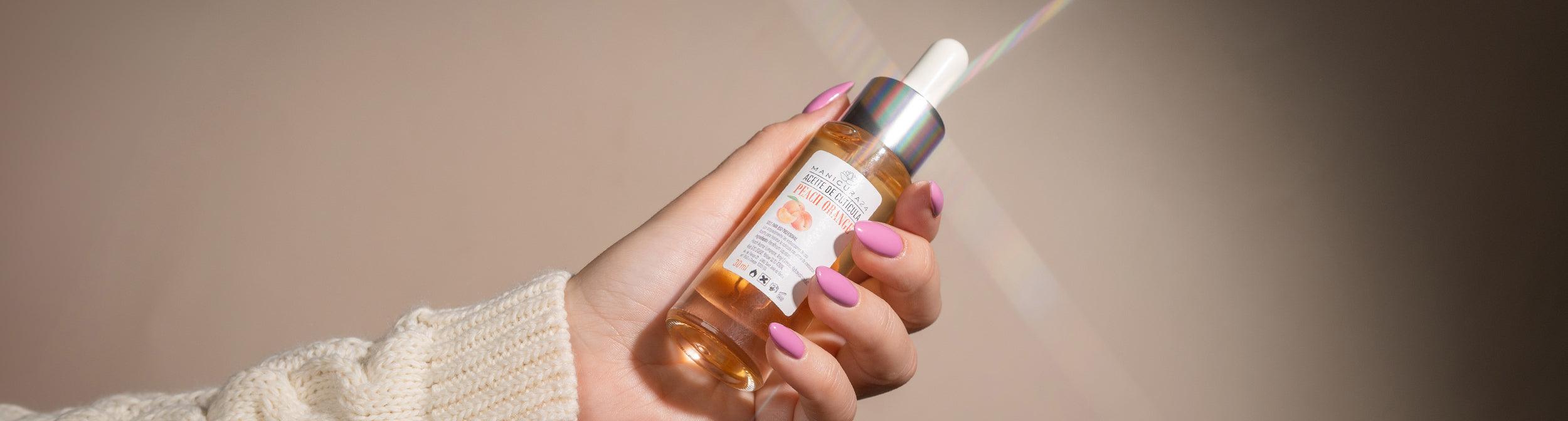 Mano con uñas esmaltadas sosteniendo aceite de cutícula para manicura profesional