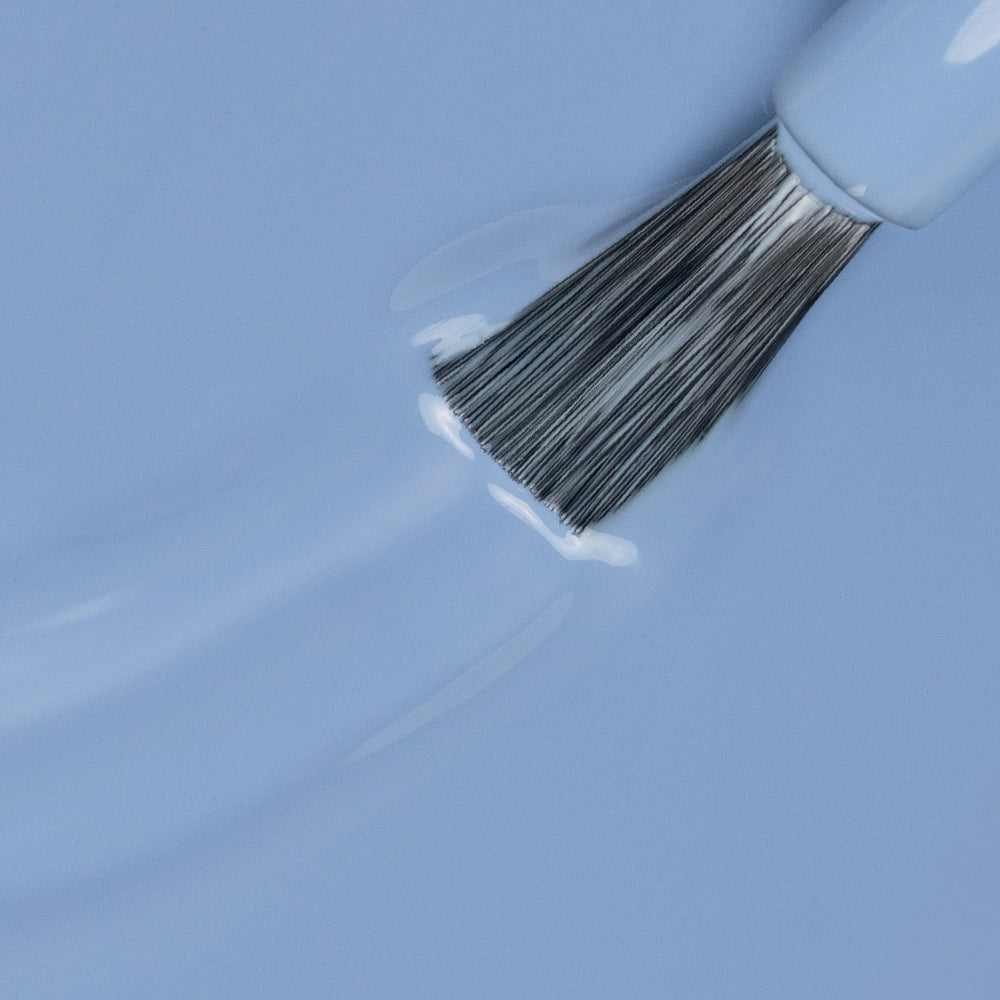 Brocha aplicando esmalte de uñas color azul claro, manicura profesional.