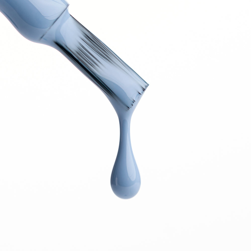 Brocha de esmalte de uñas con gota de gel azul grisáceo, fondo blanco, manicura profesional